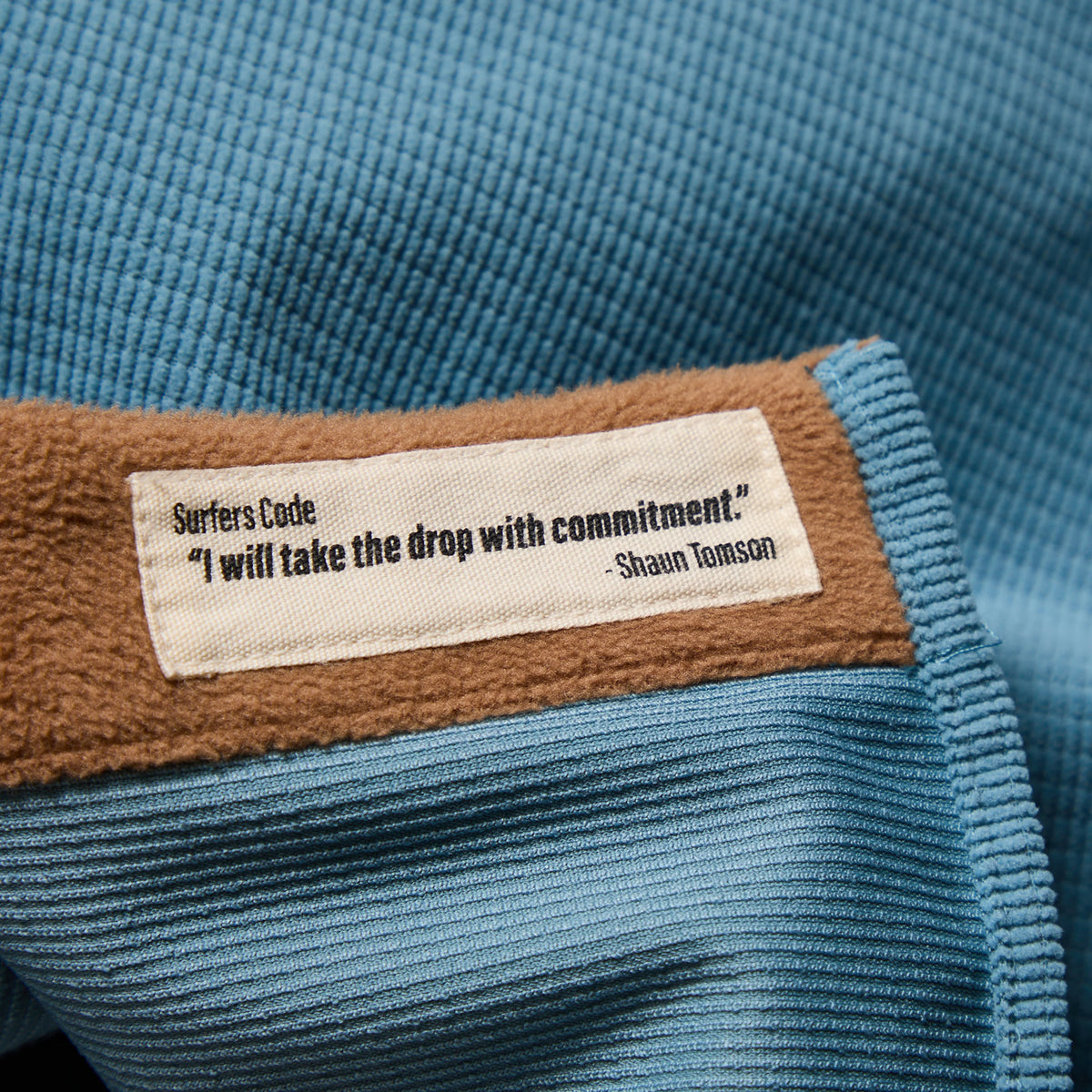 Inside woven label on blue shirt jacket collar with brown patch detail