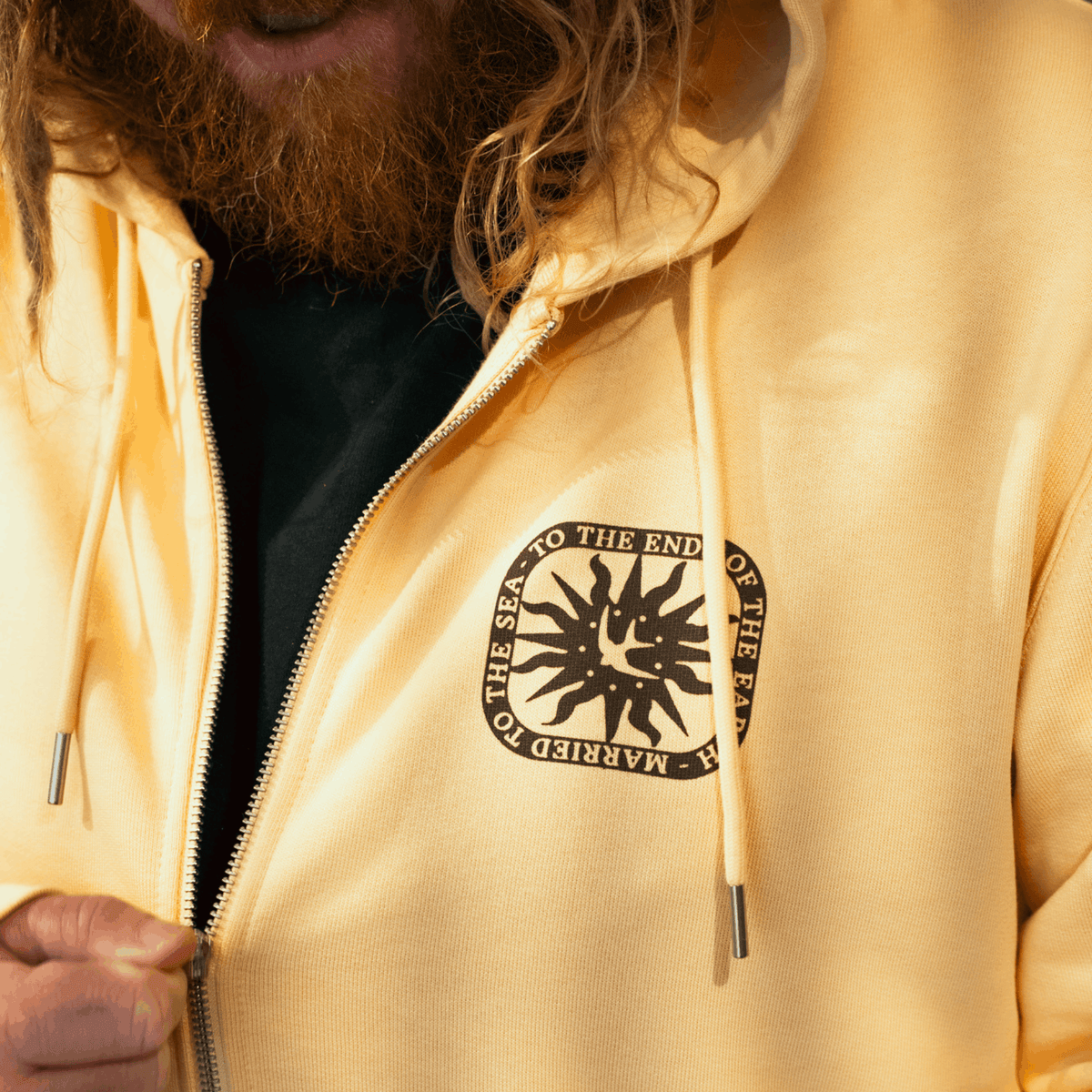 Yellow zip hoodie with front logo patch and drawstring hood, close-up